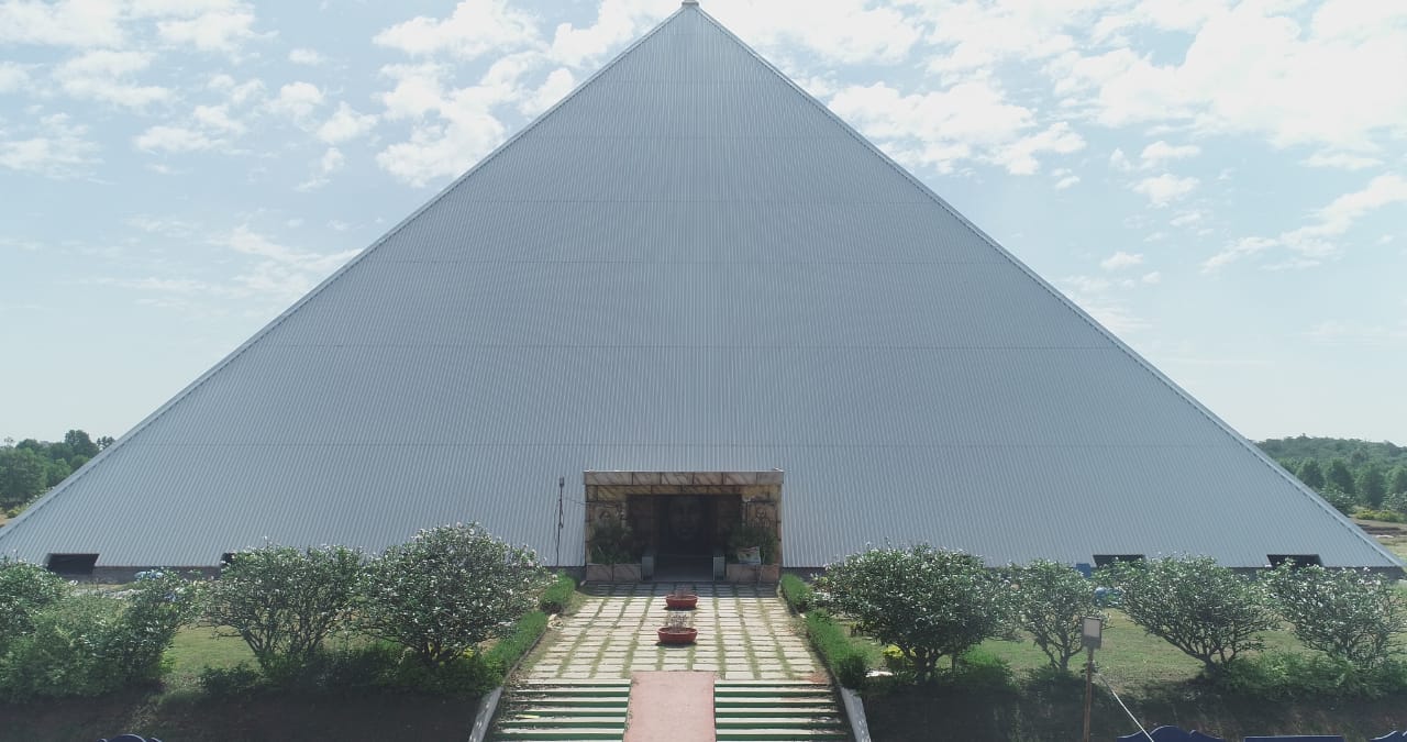 Pyramid entrance with stone-framed doorway and landscaped hedges