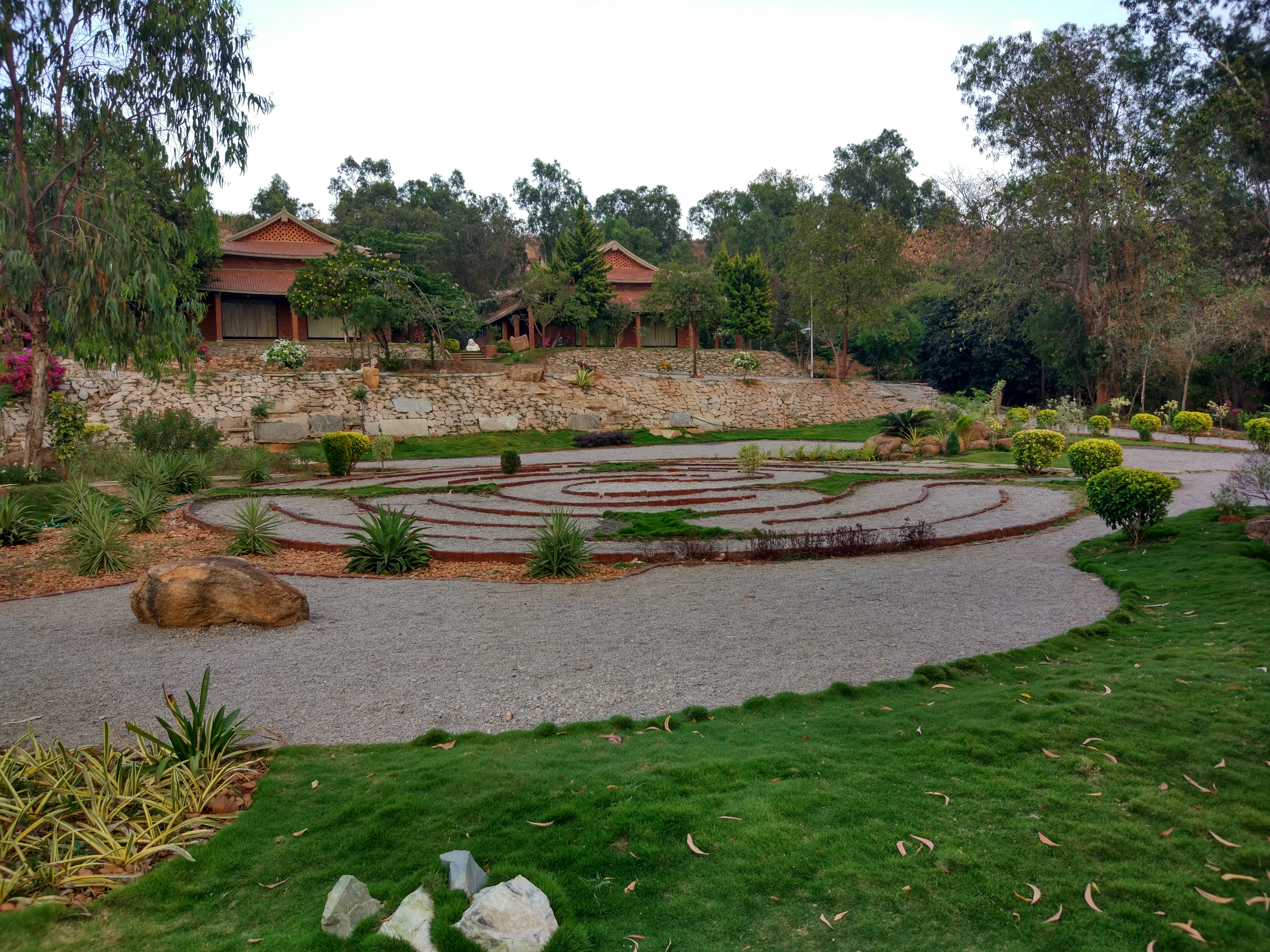 Circular gravel labyrinth in the campus garden with tiled-roof accommodation beyond