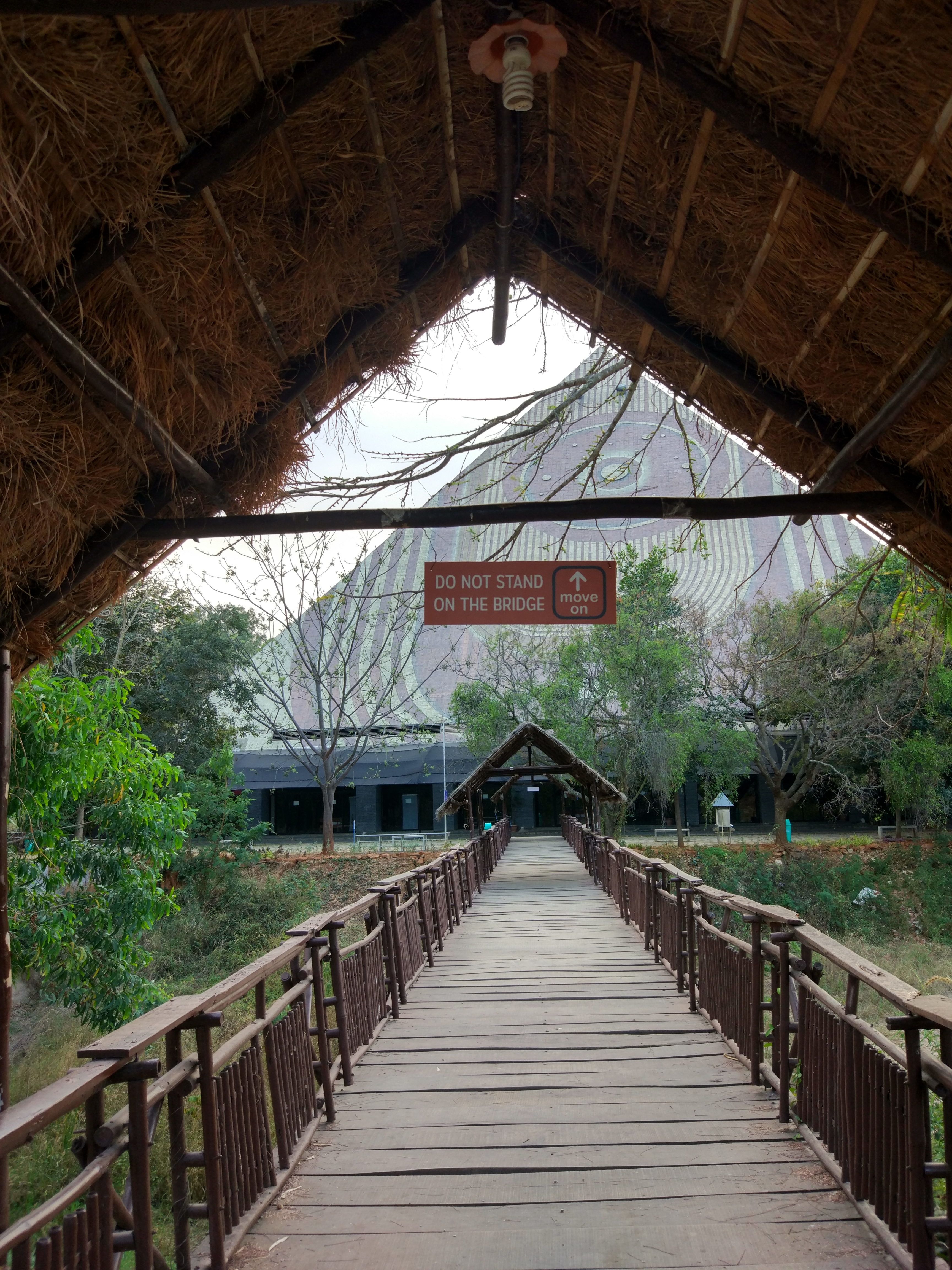 Thatched-roof gateway framing the approach bridge to the pyramid