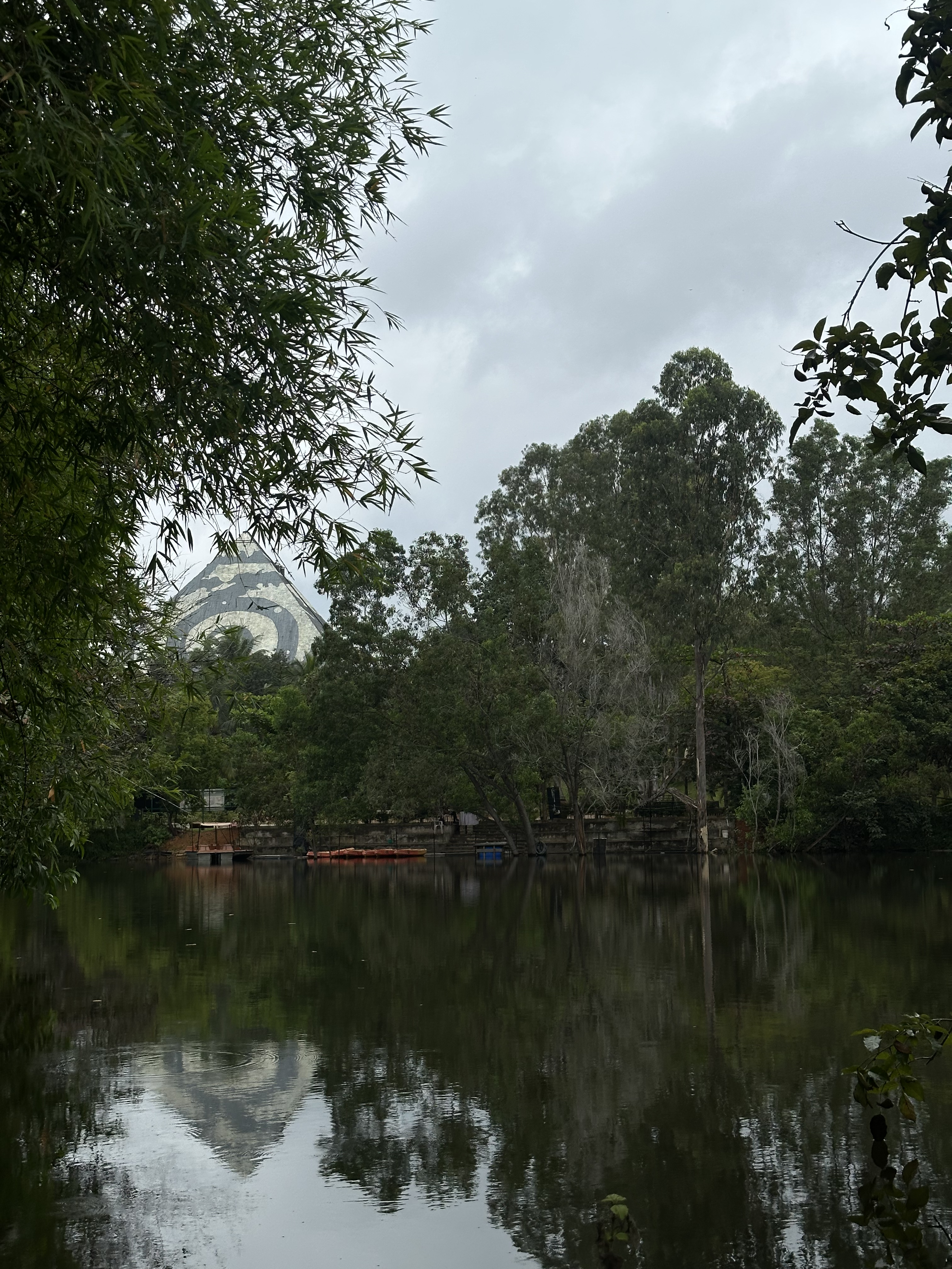 Maitreya Buddha Pyramid reflected in a still lake, framed by overhanging tree branches