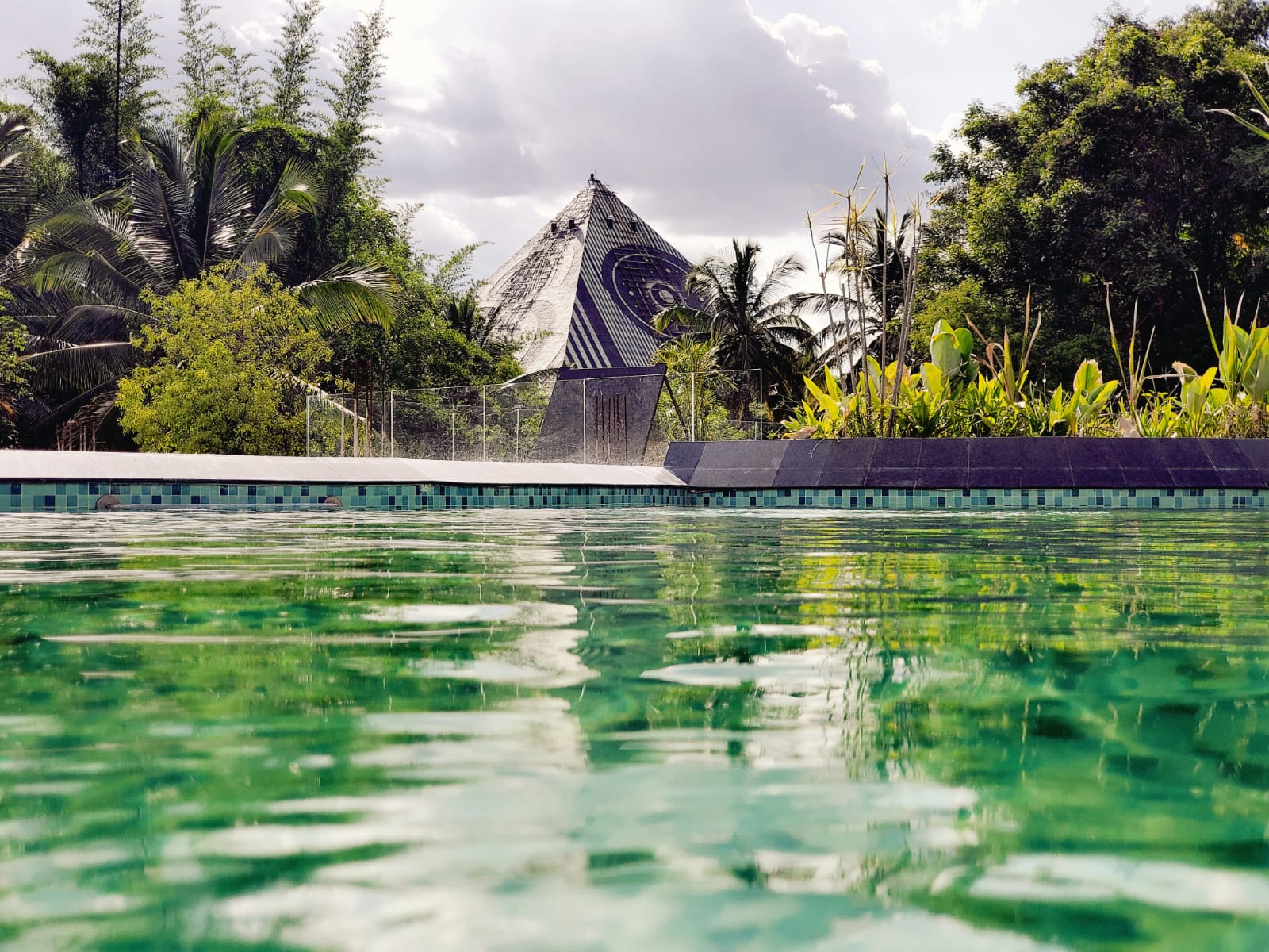 Pool edge with tiled coping and pyramid glimpsed through tropical planting
