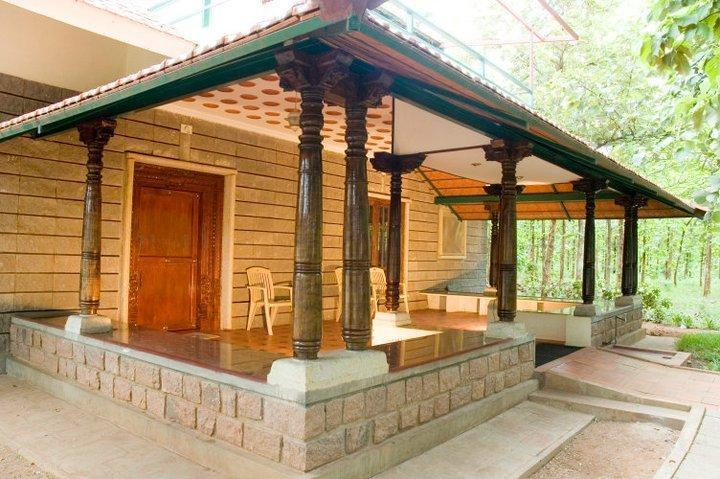 Verandah with carved wooden pillars on a granite plinth, forest beyond