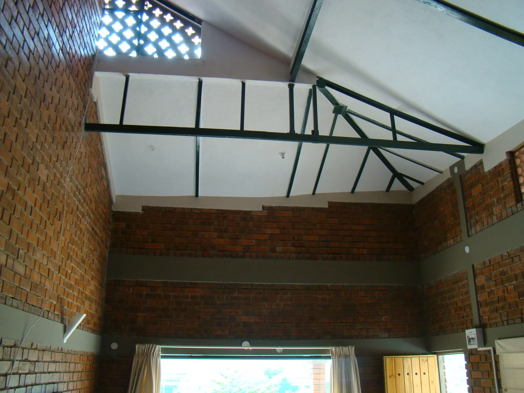 A double-height brick room with a steel truss roof and jaali clerestory