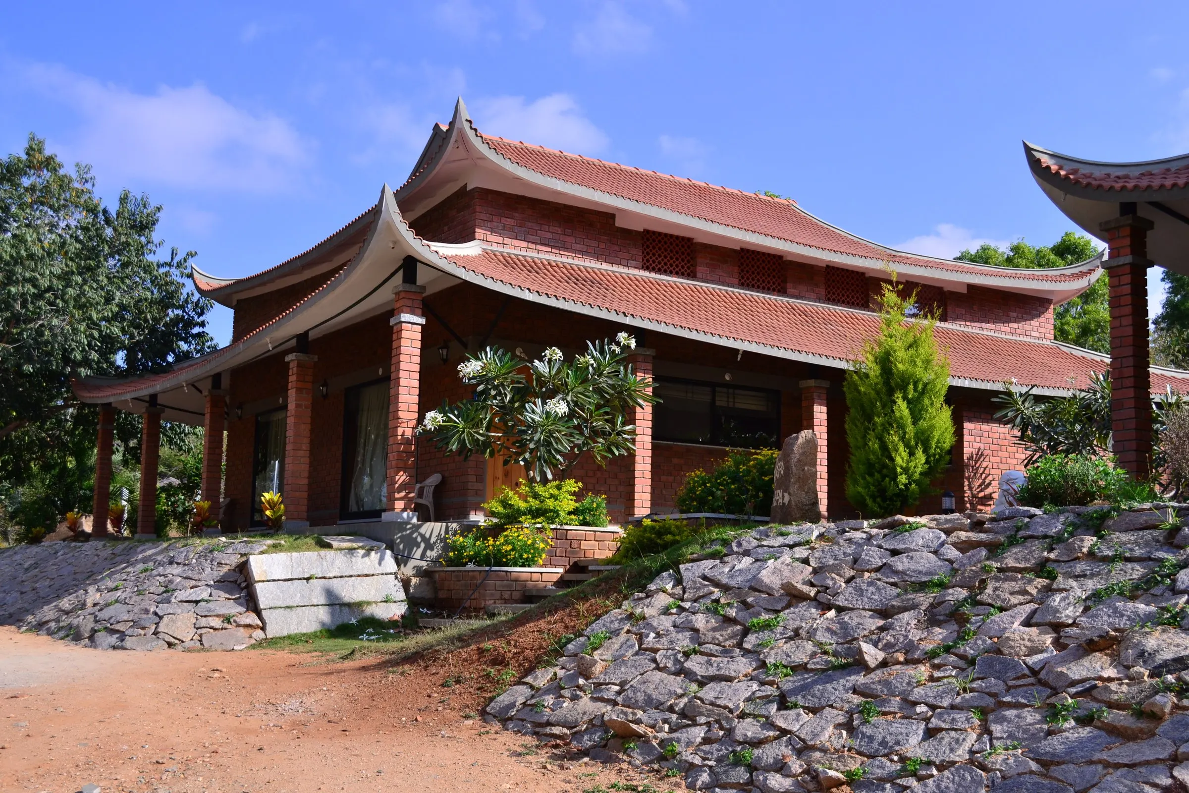 A brick cottage under sweeping pagoda roofs, set on a rubble slope against a blue sky