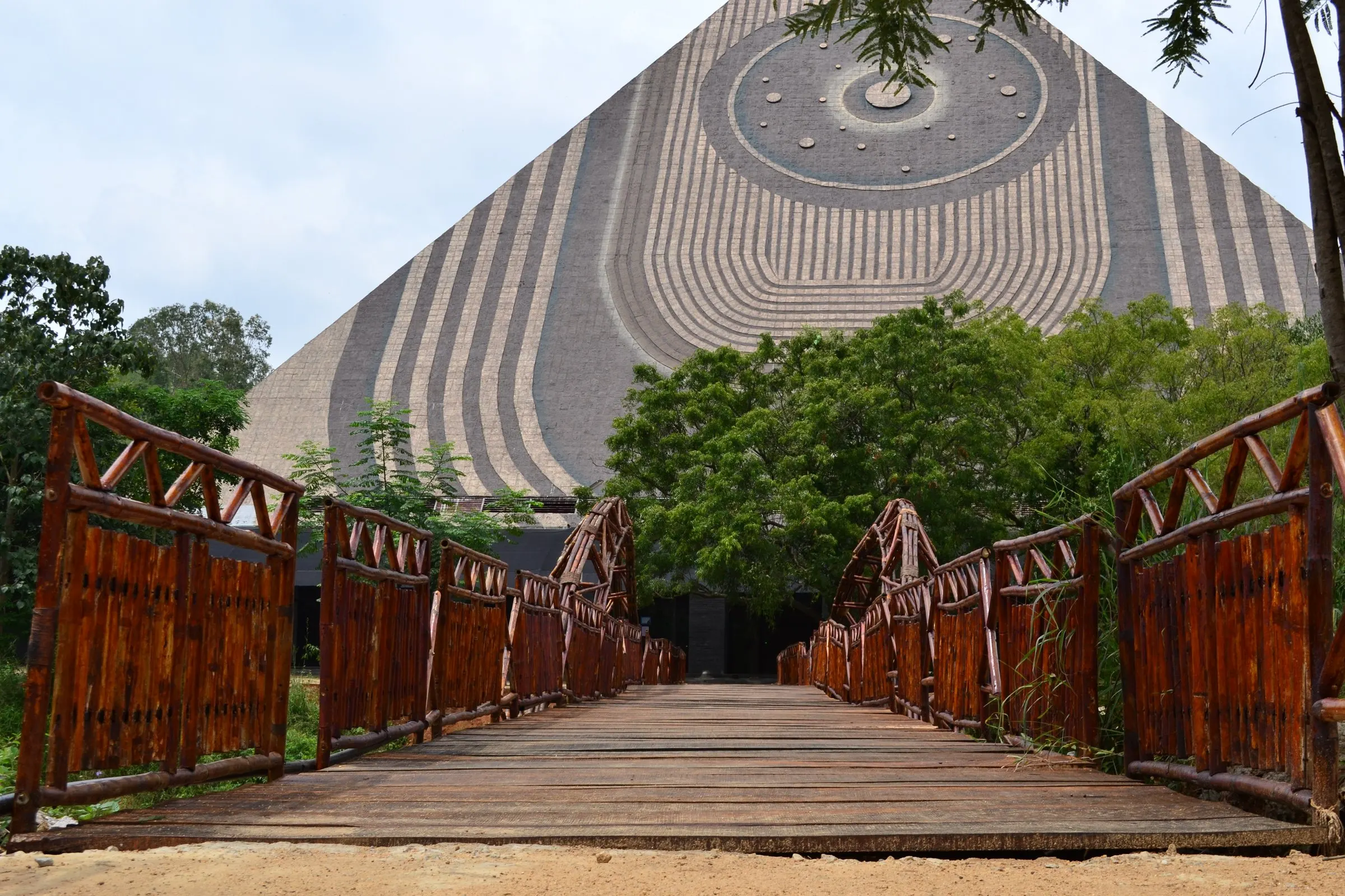A timber footbridge with railings leading straight to the base of the Pyramid Valley meditation pyramid