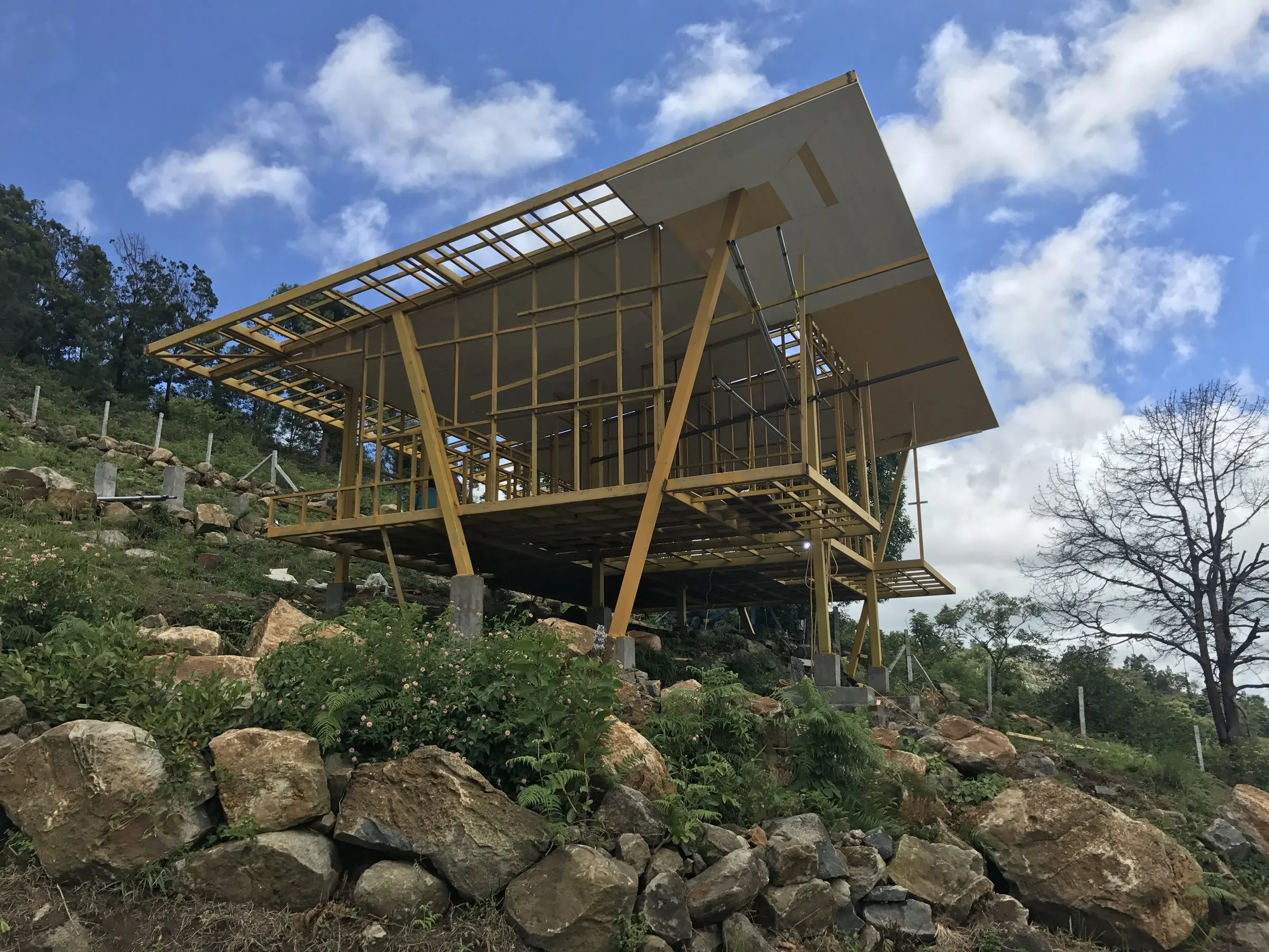 A stilted timber-and-steel cottage frame standing on a rocky hillside